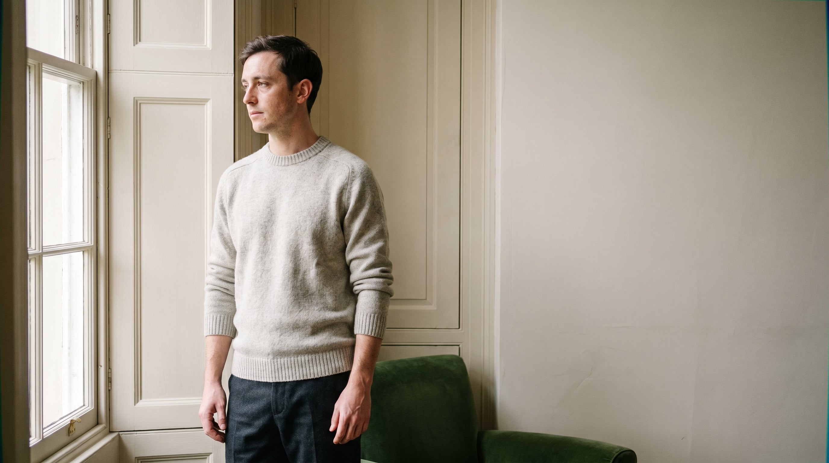 A man in a well-fitted grey crew-neck knit by a window